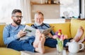 An adult hipster son and senior father sitting on sofa indoors at home, talking. Royalty Free Stock Photo