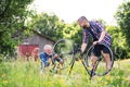 An adult hipster son and senior father repairing bicycle outside on a sunny day.