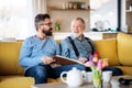 An adult hipster son and senior father sitting on sofa indoors at home, talking. Royalty Free Stock Photo