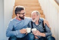 An adult hipster son and senior father sitting on stairs indoors at home, talking. Royalty Free Stock Photo