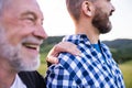 An adult hipster son with senior father on a walk in nature at sunset.