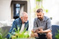 An adult hipster son with tablet and senior father in a cafe in town.