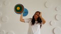 Young woman lifts multicolored barbell against white patterned wall. Adult lady doing sport, using all her strength