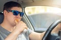 Adult male caucasian person eating hot dog fast food snack while driving car on sunny day. Men hsving food while driving steering