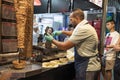 an adult male chef with a stylish hairstyle and beard is preparing a shawarma on the street. He slices fried meat to put