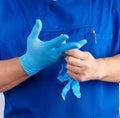Adult male doctor in blue uniform puts on his hands blue sterile latex gloves