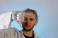 An adult male dressed in a white lab coat with a hair net on. He is unhappy and giving a thumbs down. He is ready to work in a