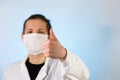 An adult male dressed in a white lab coat with a protective face mask on while giving a thumbs up. Ready to work in a clean room