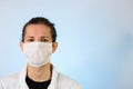 An adult male dressed in a white lab coat with a protective face mask on. Ready to work in a clean room or laboratory