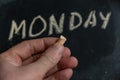 Adult male holding a piece of yellow chalk in his hand. Handwritten word MONDAY on black chalkboard. Days of the week. Calendar