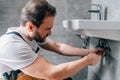 Adult male plumber in working overall fixing sink