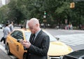 Adult male seen texting using a mobile phone next to a yellow cab near Central Park, NYC.