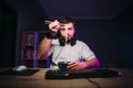 An adult man with a beard sits at the computer at night at work and eats Chinese food with chopsticks, holding noodles on sticks Royalty Free Stock Photo