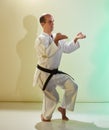 An adult man with a black belt performs formal exercises against a colored background with yellow and green tints Royalty Free Stock Photo