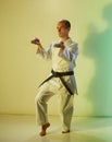 Adult man with black belt training formal exercises against color background with yellow and green tint Royalty Free Stock Photo