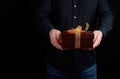 Adult man in a black shirt holds a red square box with a knotted bow on a dark background Royalty Free Stock Photo