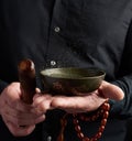 Adult man in a black shirt rotates a wooden stick around a copper Tibetan bowl of water. ritual of meditation Royalty Free Stock Photo
