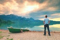 Adult man in blue shirt walk at old fishing paddle boat at mountains lake coast. Royalty Free Stock Photo