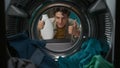 View from inside the washing machine, adult man with laundry basket holding a bottle of softener Royalty Free Stock Photo