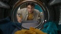 View from inside the washing machine, adult man with laundry basket takes out clothes from the drum Royalty Free Stock Photo