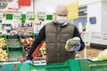 Adult man choosing vegetables at a supermarket with gloves and a mask on. Conscientious shopping during the virus outbreak