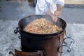 The cook mixes pilaf in a cauldron during cooking