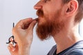 Man cutting his own beard and mustache with scissors and comb. Caucasian red bearded male trimming hair on face at home Royalty Free Stock Photo