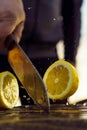 Adult man cutting lemon in half with knife. Human separate into pieces juicy and sour fruit that lie on table.