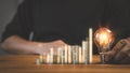 Adult man hand holding a light bulb and money stack on table.