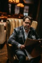 Mid-aged well-dressed man sitting in arm-chair in living room reads newspaper Royalty Free Stock Photo