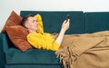Adult man lie on sofa and watch video on smartphone, side view. Person reclining on pillow under blanket and lounging.