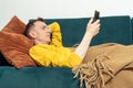 Adult man lie on sofa and watch video on smartphone, side view. Person reclining on pillow under blanket and lounging.