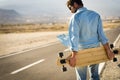 Adult man with long board table walking on a long asphalt street - concept of alternative modern people and travel transport free