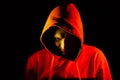 An adult man looks out from under the hood with a grin like a psycho or a maniac in an orange hooded sweatshirt highlighted in red Royalty Free Stock Photo