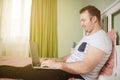 Adult man lying in his bed while he is working from home on his laptop Royalty Free Stock Photo