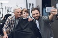 Adult man makes selfie on a smartphone with older men and boy in barbershop. Royalty Free Stock Photo