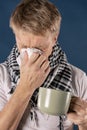 Man in a checkered scarf with big mug and tissue on blue background. Cold and flu illness relief Royalty Free Stock Photo