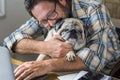 Adult man play with his best friend old dog pug in the office at home - concept of couple people animals and love friendship - Royalty Free Stock Photo