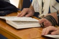 An adult man pointing at a phrase in a bible book sefer torah, while reading a pray