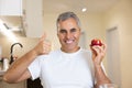 Adult man prefers healthy food. Light smart interior on background. Mature man holds red fresh apple, thumbs up and