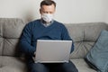 Adult man in protective medical mask work at home by laptop. Remote work. Covid-19. Quarantine. Stay at home Royalty Free Stock Photo