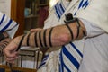 An adult man putting a Jewish Tefillin on his arm and wearing prayer shawl for praying