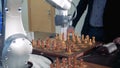 An adult man and a robotized arm are playing chess and moving pieces