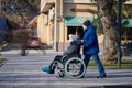 Adult man rolls his disabled mother on wheelchair, careful relationships with disabled person