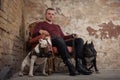 Adult man satting in a vintage armchair on the background of a peeled wall. On each side the man sitting two dogs. black pit bull Royalty Free Stock Photo