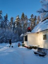 An adult man shovels snow from the roof of the veranda of a country house with a shovel, a young man removes snow below, a girl