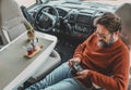 Adult man sitting inside motor home camper van cabin using photo camera and drinking coffee. Concept of travel and adventure