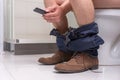 Adult man using phone while sitting on a toilet bowl