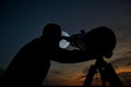 Adult man using a telescope at sunset time observing the moon at night. Amateur astronomy concept with empty copy space