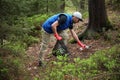 Adult man volunteer in red gloves removes plastic trash in forest, caring for environment